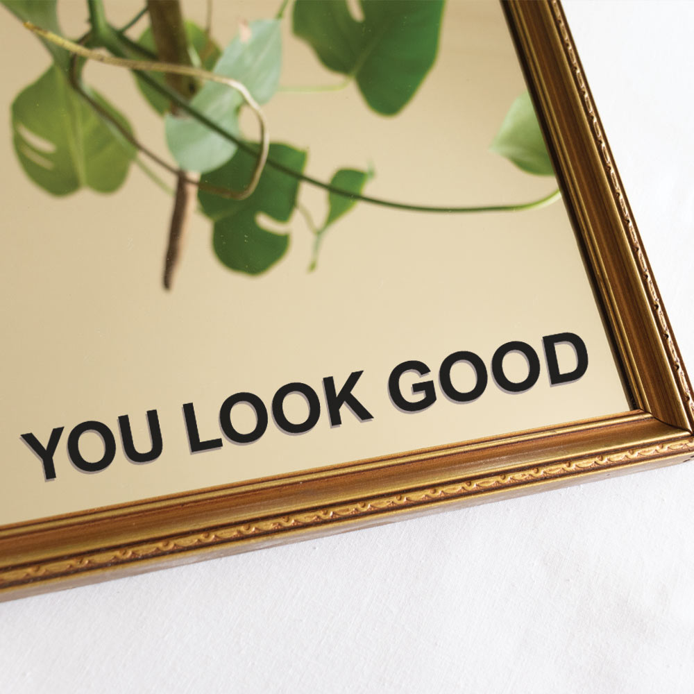A gold-framed mirror with the decal 'YOU LOOK GOOD' printed in black across the bottom.