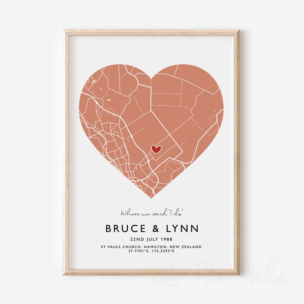 Framed orange and white heart-shaped map print with text personalization.

A red heart marks a specific location. 
Small cursive headline text reads " Where we said "i do"". Secondary capitalized text (slightly larger) below that reads " Bruce & Lynn"  and then a personalised special date, location and map coordinates. 